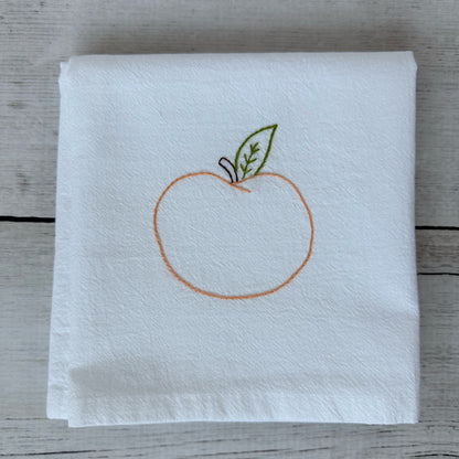 White tea towel with embroidered peach design on a wooden surface