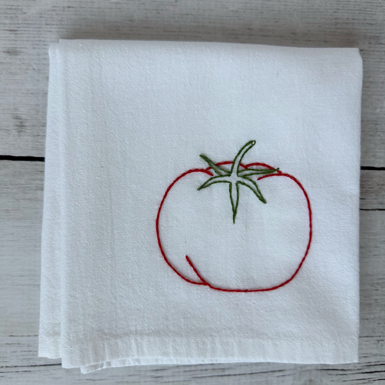 White tea towel with red embroidered tomato design on a wooden surface