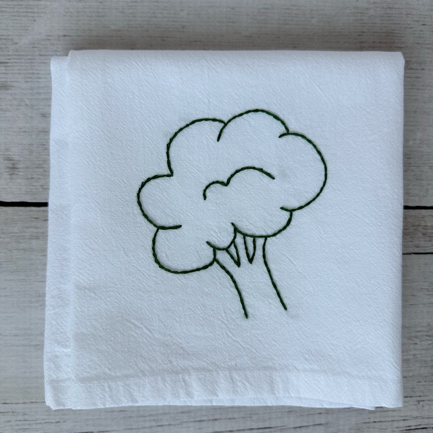 White tea towel with embroidered broccoli design on a wooden surface