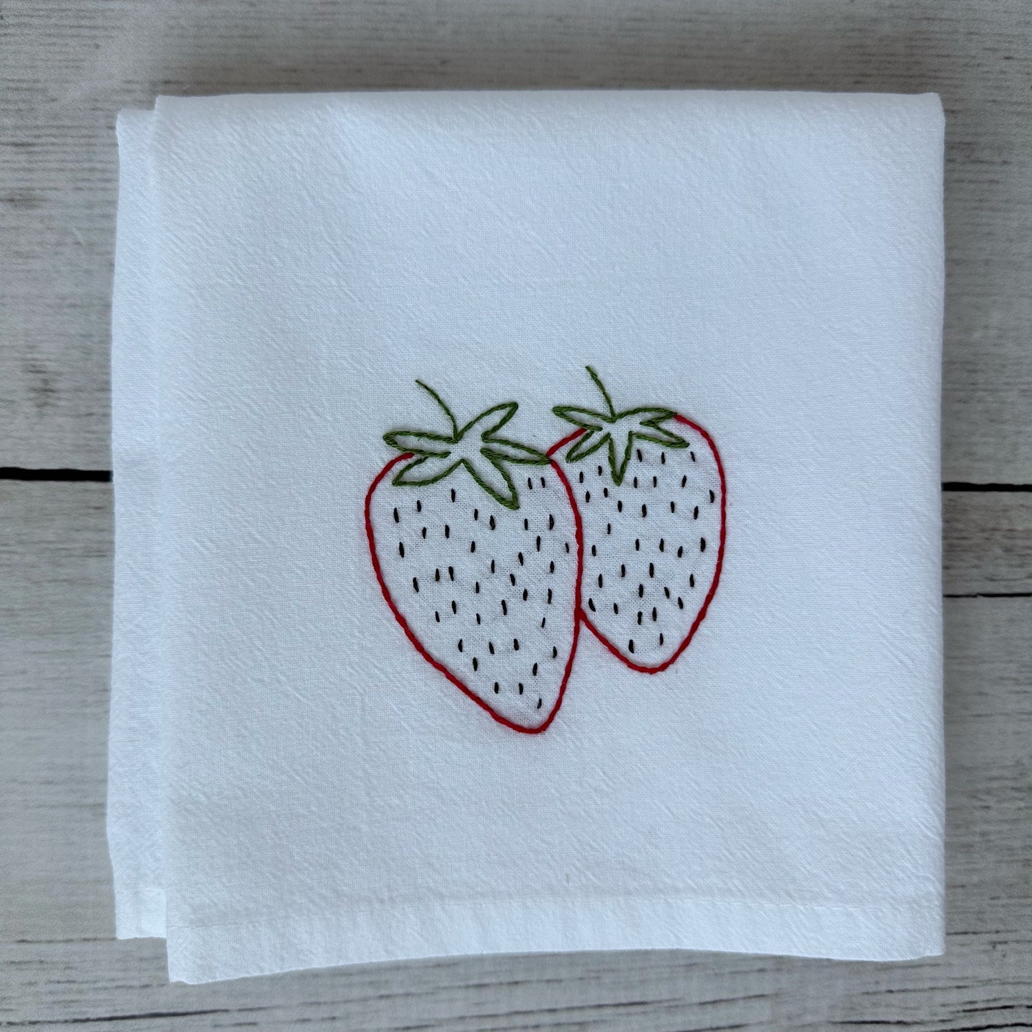 White tea towel with embroidered strawberries on a wooden surface
