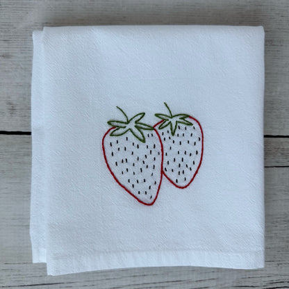 White tea towel with embroidered strawberries on a wooden surface