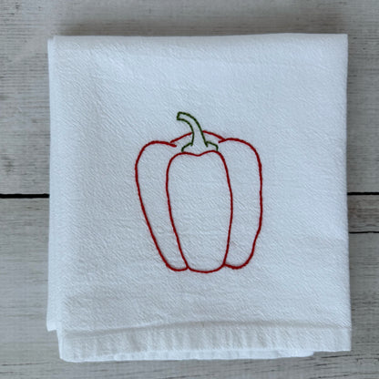White tea towel with embroidered red bell pepper design on a wooden surface