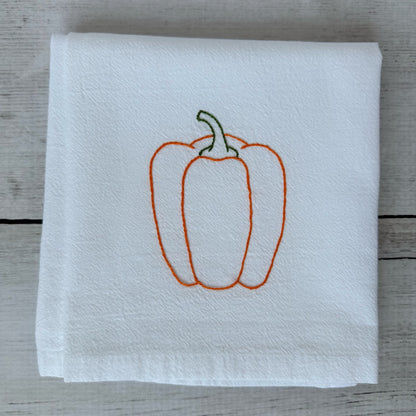 White tea towel with embroidered orange bell pepper design on a wooden surface