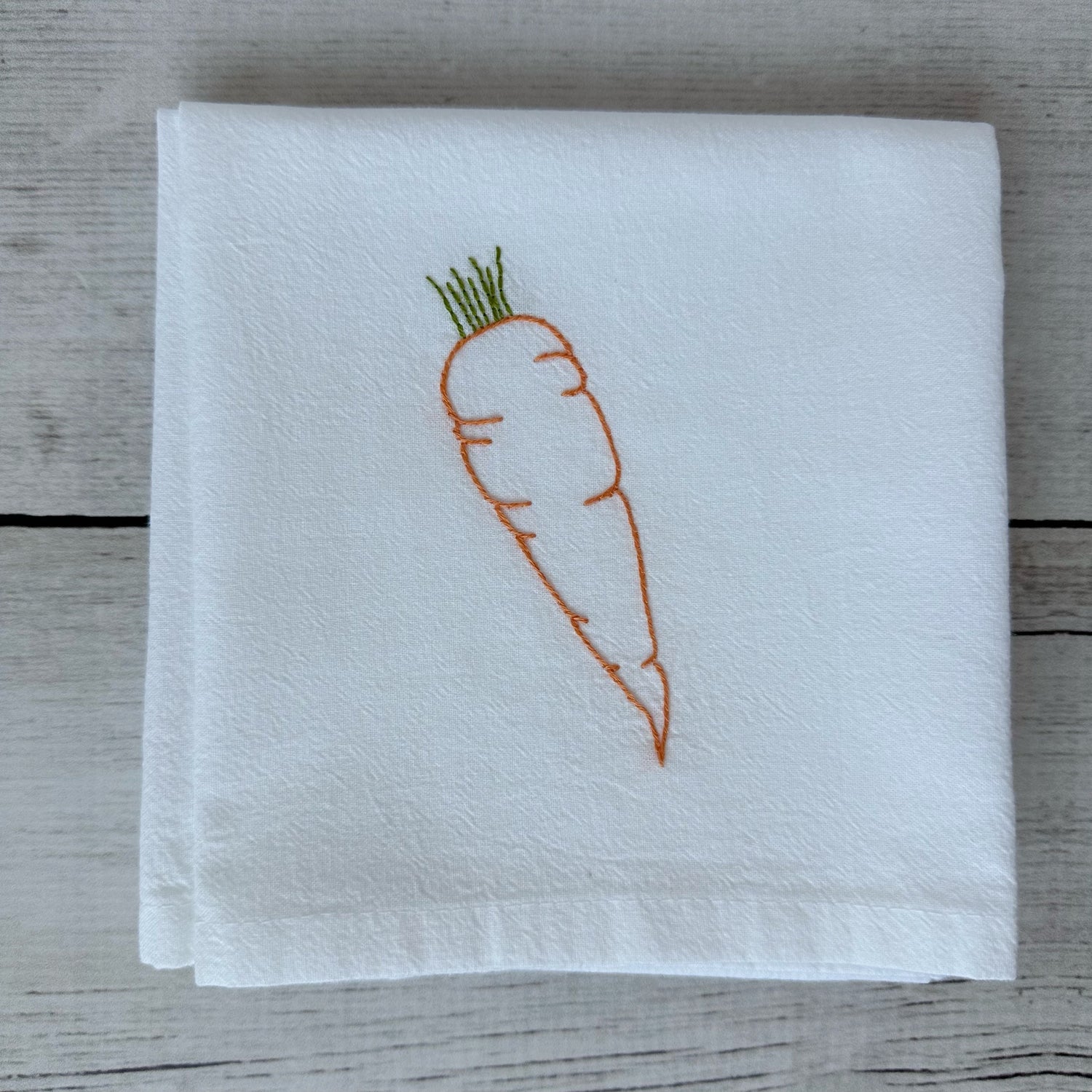 White tea towel with embroidered carrot design on a wooden surface