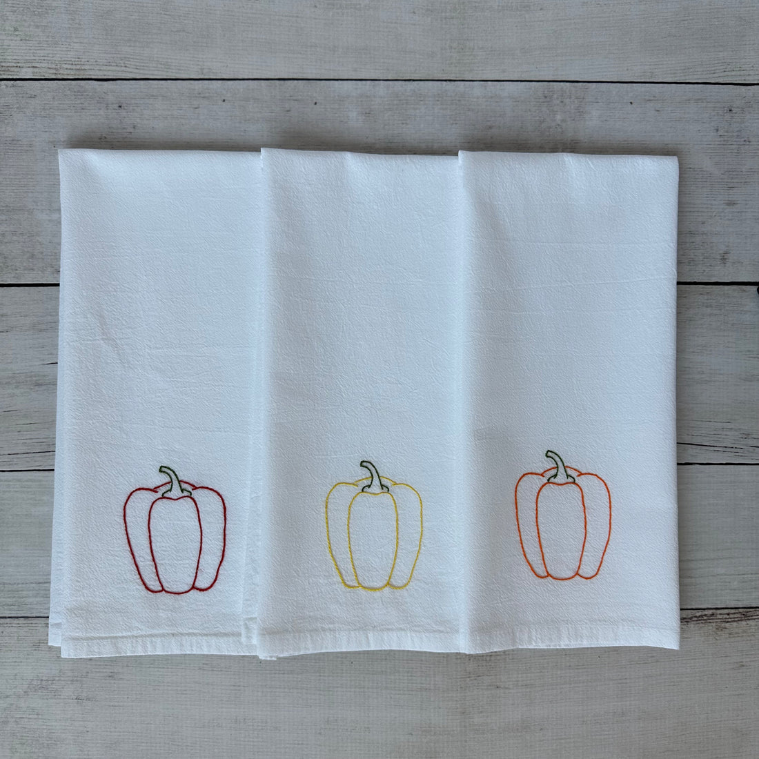 White tea towel with embroidered bell pepper designs on a wooden surface