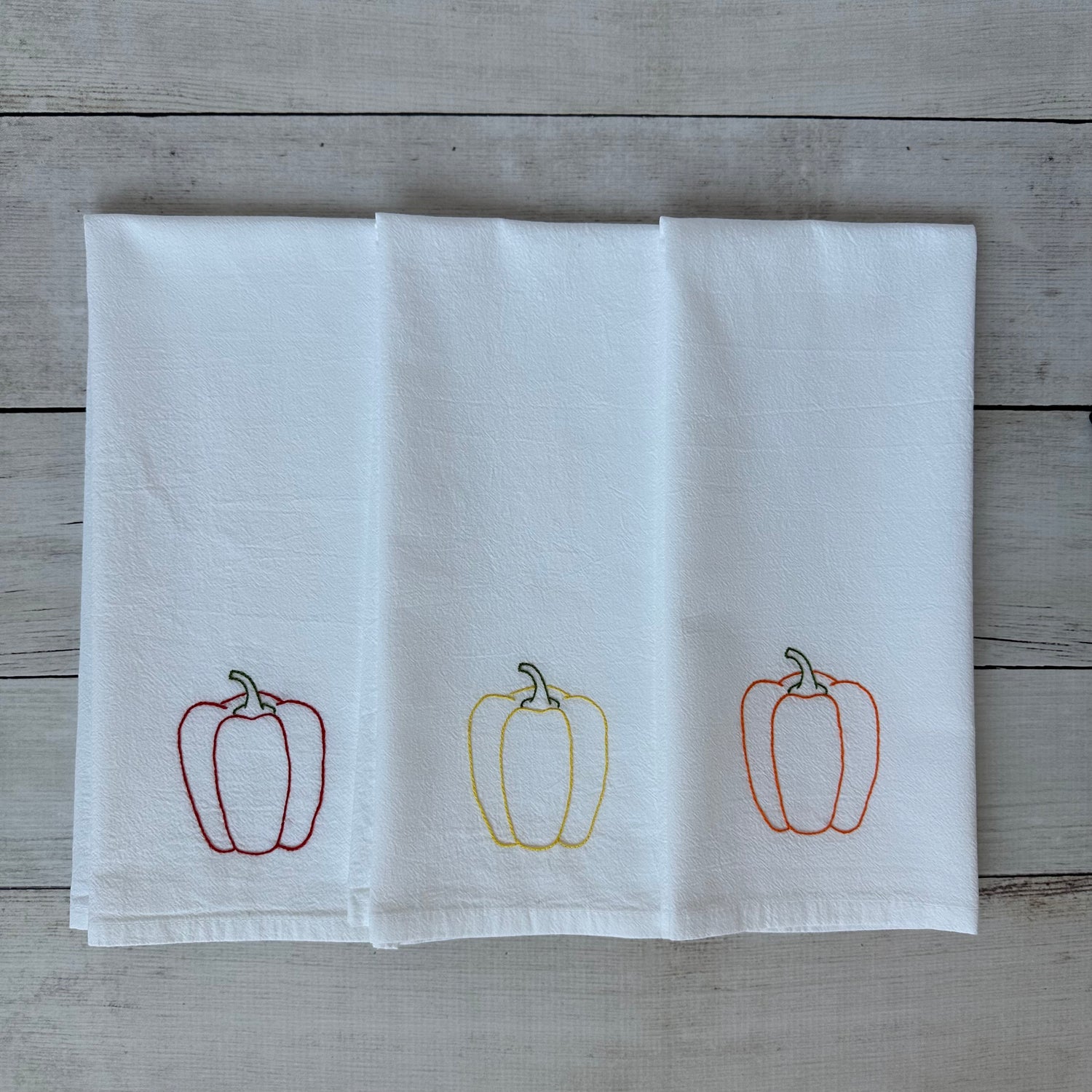 White tea towel with embroidered bell pepper designs on a wooden surface