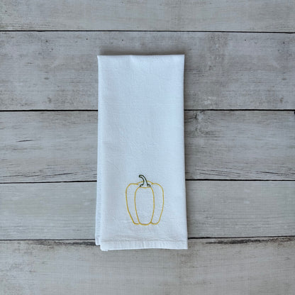 White tea towel with embroidered yellow bell pepper design on a wooden surface