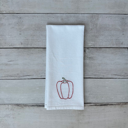 White tea towel with embroidered red bell pepper design on a wooden surface