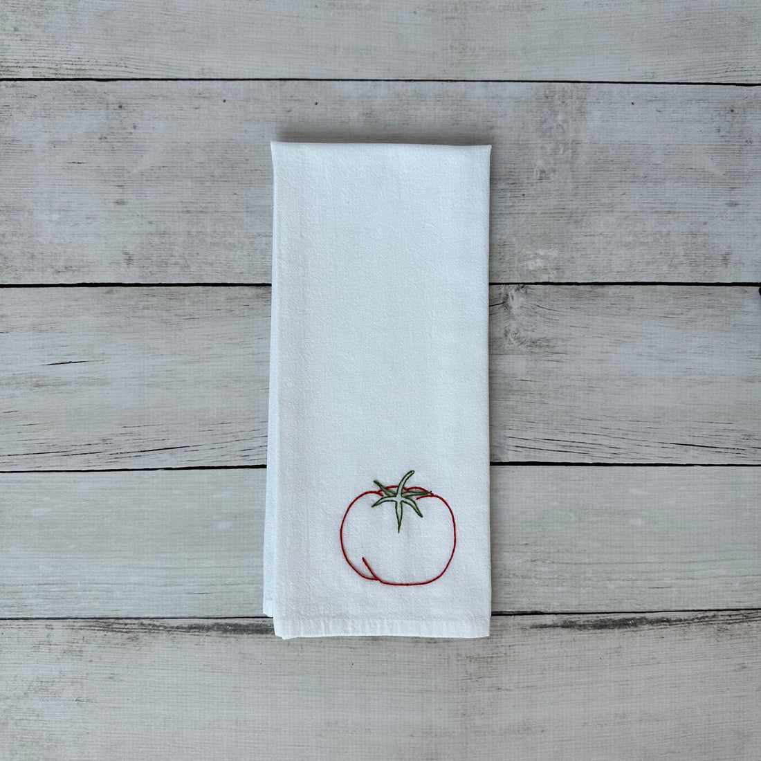 White tea towel with a tomato design on a wooden surface