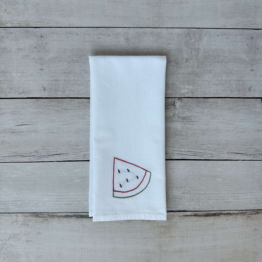White tea towel with embroidered watermelon design on a wooden surface