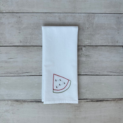 White tea towel with embroidered watermelon design on a wooden surface