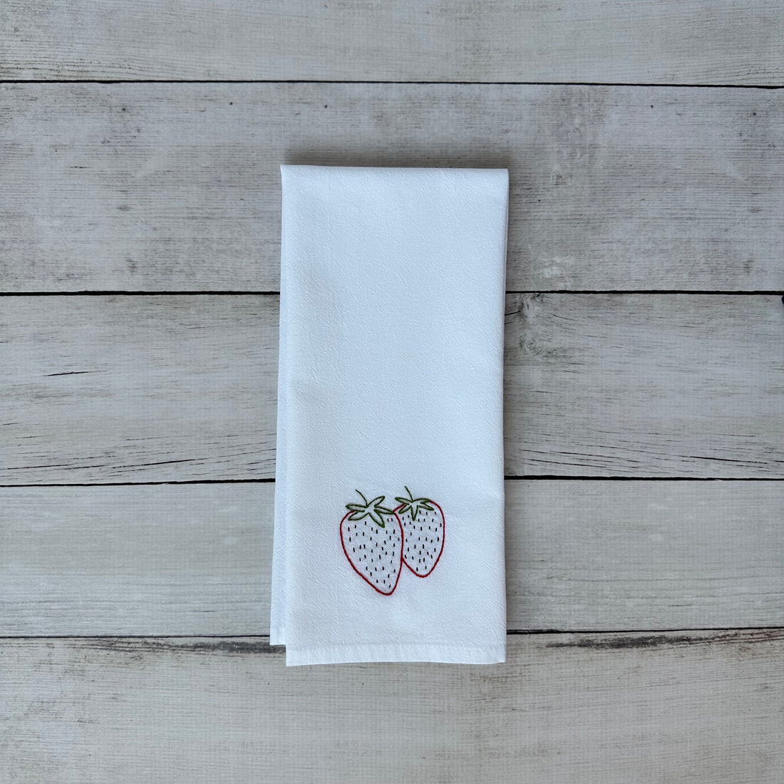 White tea towel with embroidered strawberry design on a wooden surface