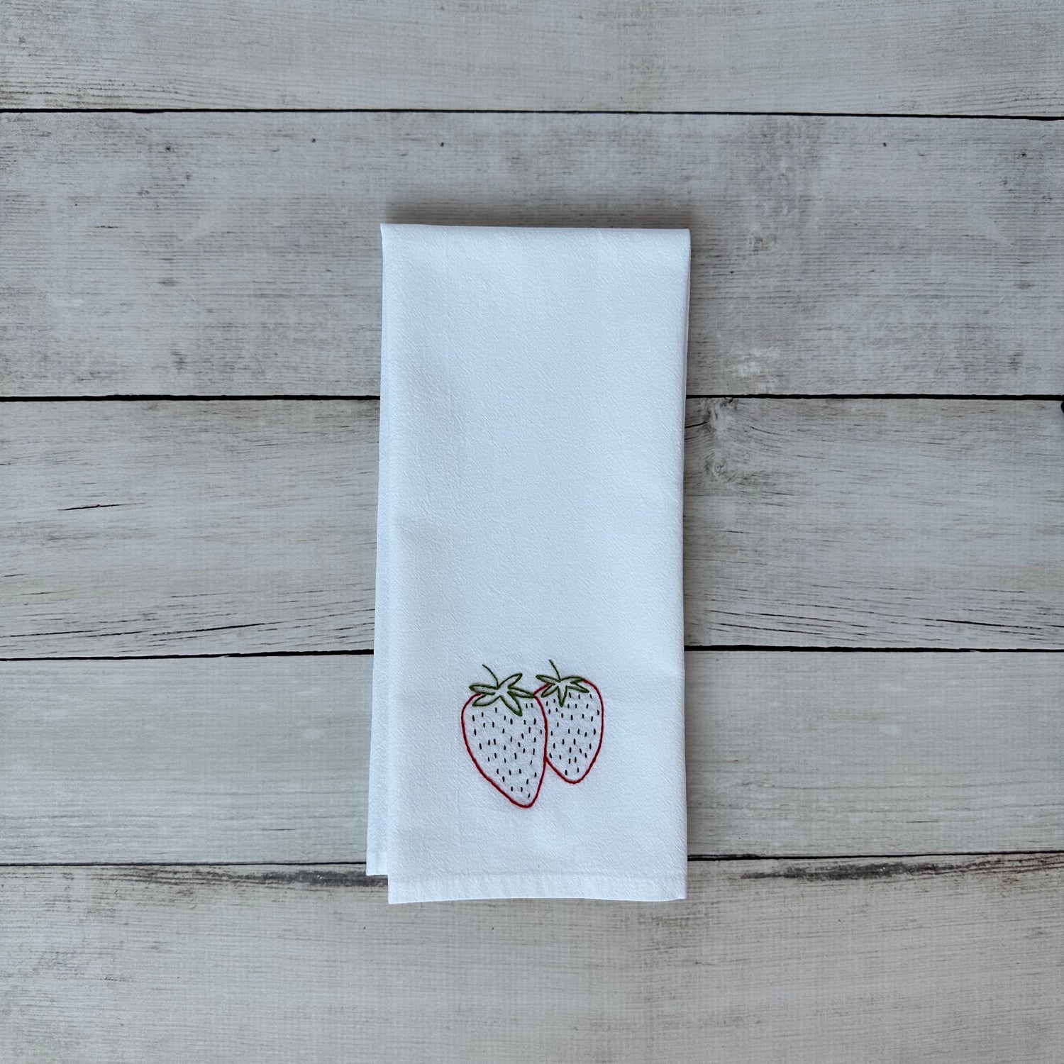 White tea towel with embroidered strawberry design on a wooden surface
