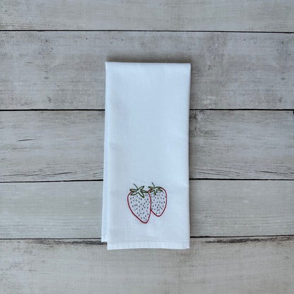 White tea towel with embroidered strawberry design on a wooden surface