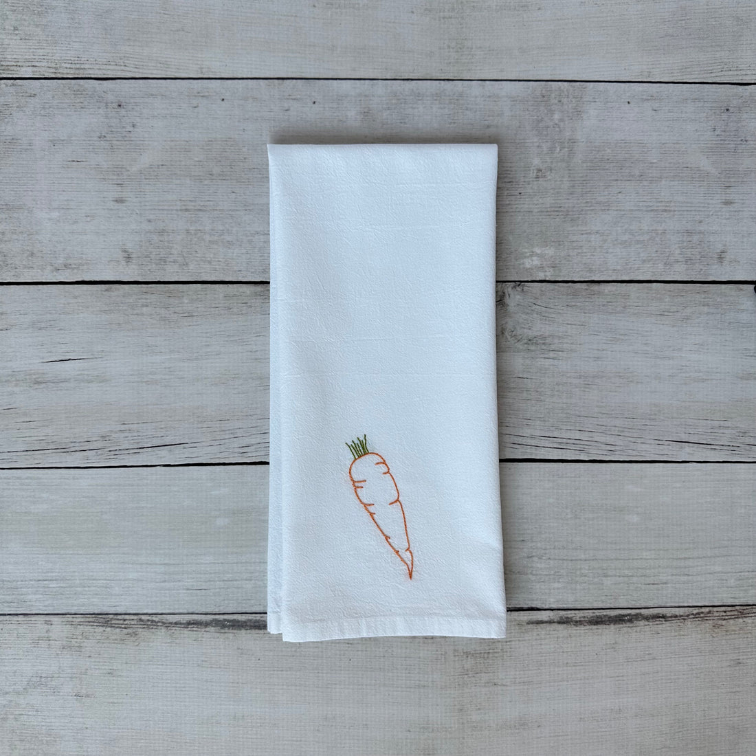 White tea towel with embroidered carrot design on a wooden surface