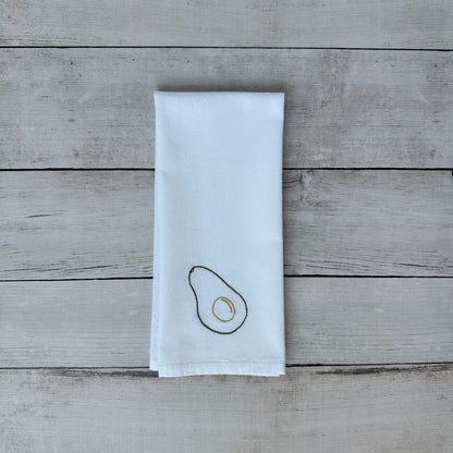 White tea towel with embroidered avocado design on a wooden surface