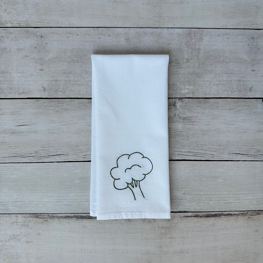 White tea towel with embroidered broccoli design on a wooden surface