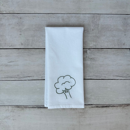 White tea towel with embroidered broccoli design on a wooden surface