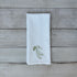 White tea towel with embroidered snap peas on a wooden surface