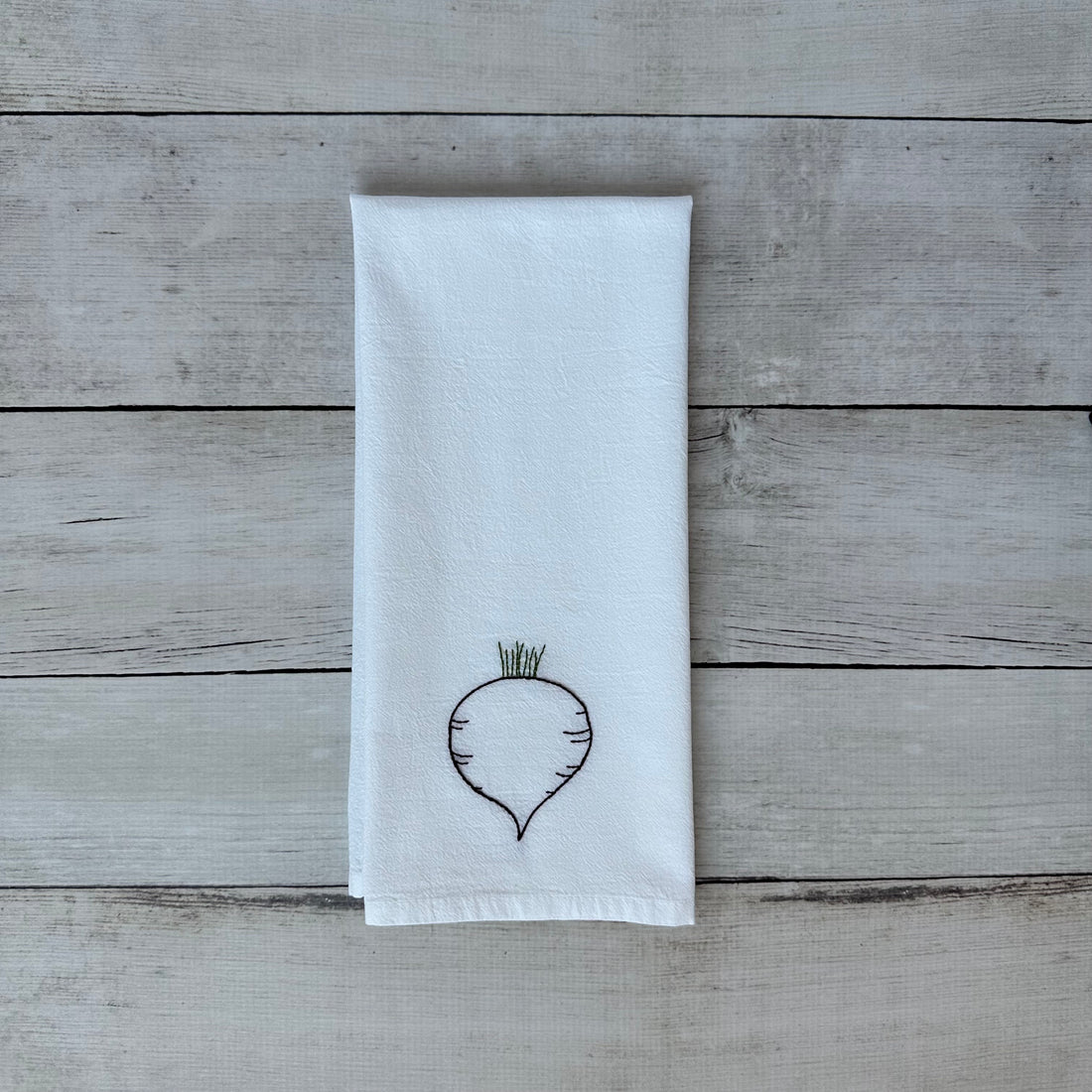 White tea towel with embroidered beet design on a wooden surface