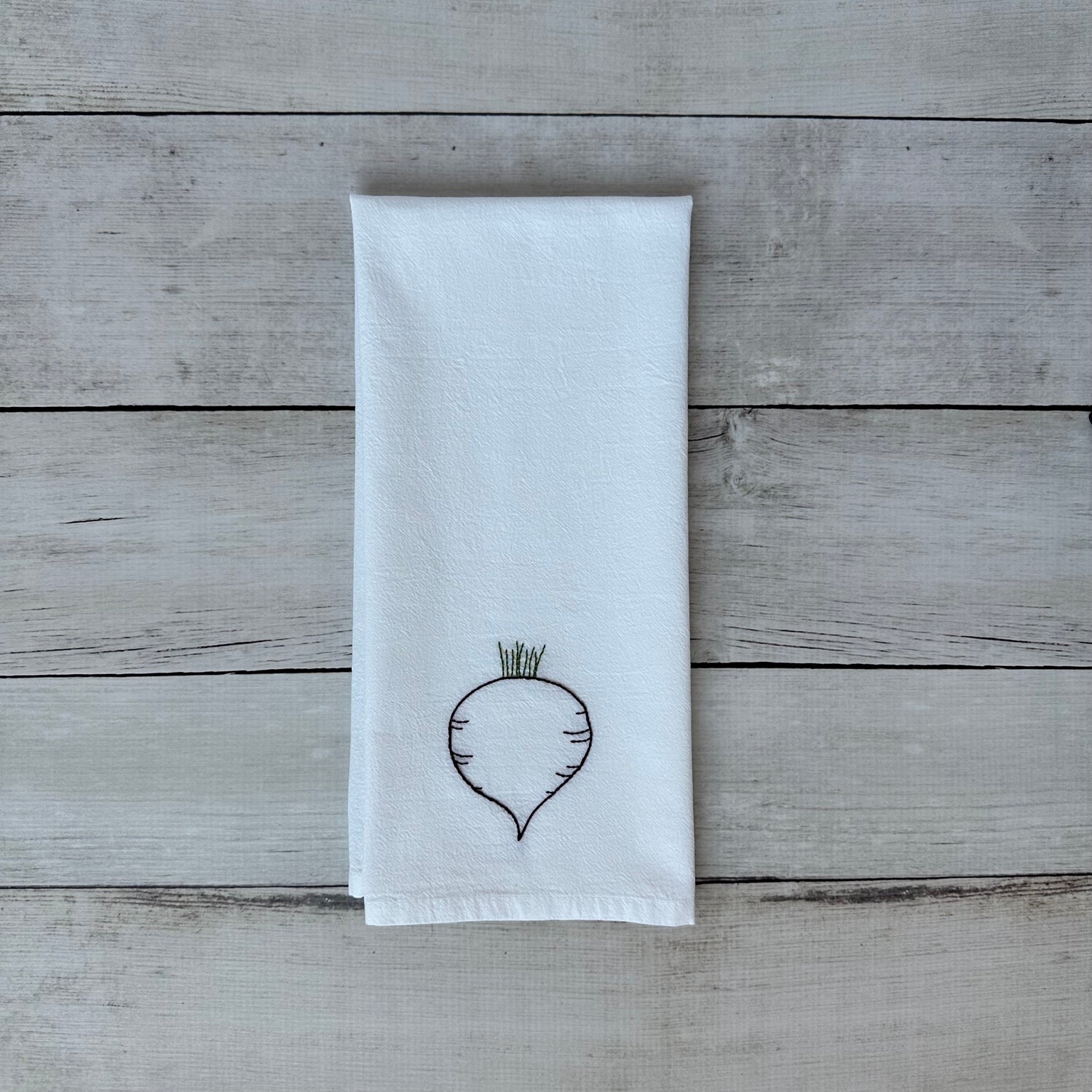 White tea towel with embroidered beet design on a wooden surface