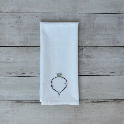 White tea towel with embroidered beet design on a wooden surface